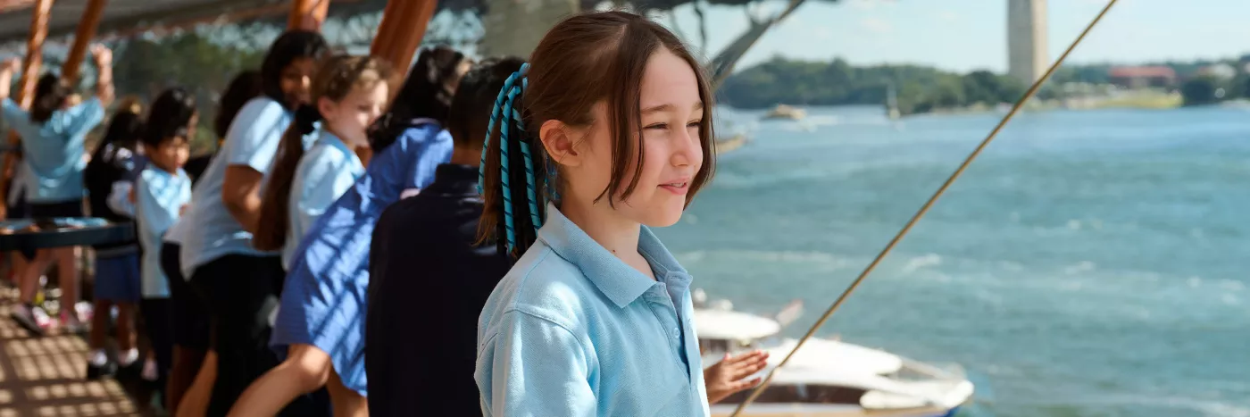 A young girl wearing a school uniform stares out a window in a Sydney Opera House foyer. The Sydney Harbour Bridge is seen in the background.